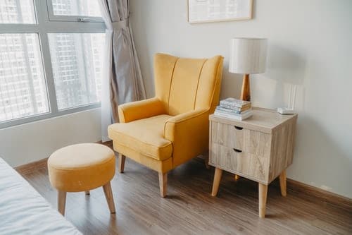 yellow armchair and stool beside wooden nightstand